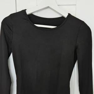 Svart långärmad bodysuit - En stilren svart långärmad bodysuit med rund halsringning. Perfekt att styla till olika outfits och enkel att matcha med både jeans och kjol. Mjuk och stretchig känsla.