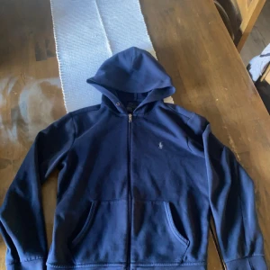 Mörkblå hoodie från Ralph Lauren - Säljer en mörkblå Ralph Lauren hoodie med dragkedja framtill och klassisk logga på bröstet