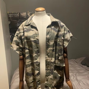 Oversized camo skjorta - Säljer en oversized skjorta med klassiskt camouflage-mönster. Skjortan har korta ärmar, bröstficka och knappar framtill. Perfekt för dig som gillar streetwear eller vill sticka ut lite extra.