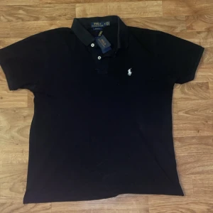 Svart pikétröja från Polo Ralph Lauren - Klassisk svart pikétröja från Polo lauren. Sparsamt använd (5 gånger) han stammar dam för den bara sitter i garderoben passar fint till sommaren.  Priset är ej hugget i sten!!