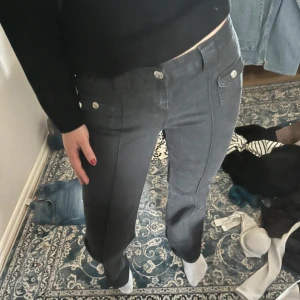 Gråa byxor med fickdetaljer - Säljer ett par gråa byxor med raka ben och dekorativa fickor framtill. Byxorna har normal passform och stängs med dragkedja och knapp. Perfekta för en stilren och enkel look. Är xs men passar även s. Är 164 o dom sitter perfekt på mih
