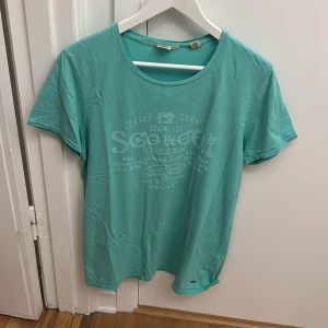 Turkos t-shirt från Scotch & Soda - Turkos t-shirt från Scotch & Soda med tryck framtill. Klassisk rund halsringning och korta ärmar. Tillverkad i mjuk bomull, perfekt för en avslappnad stil.