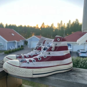 Converse All Star sneakers Stars & Stripes - Säljer ett par Converse All Star high-top sneakers med rödvita ränder och blå detaljer med vita stjärnor, inspirerat av USA:s flagga. Skorna har snörning, vit sula och klassisk rund tå. Hittade även dessa hos farmor.