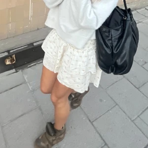 Vit volangkjol med broderade detaljer - Supersöt vit kortkjol med volanger och broderade små blommor. Elastisk midja och snygg passform.