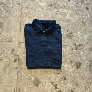 Blå piké från Polo Ralph Lauren - Säljer en klassisk blå pikétröja från Polo Ralph Lauren med röd broderad logga på bröstet. Nypris ligger på cirka 1600kr
