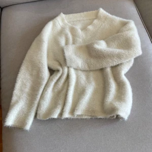 Vit fluffig stickad tröja - Mysig vit stickad tröja med fluffig känsla och lång ärm. Tröjan har en enkel design med rund halsringning och är perfekt för kyligare dagar.