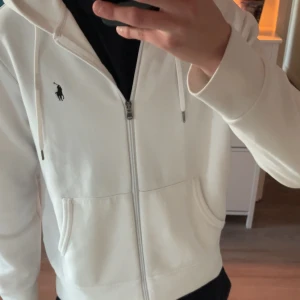 Vit hoodie med dragkedja från Polo Ralph Lauren - Säljer en stilren vit hoodie från Polo Ralph Lauren med dragkedja.