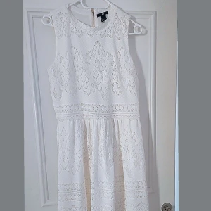 Vit spetsklänning från H&M - Säljer en elegant vit spetsklänning från H&M. Klänningen är ärmlös med en rund halsringning och har ett vackert spetsmönster. Perfekt för sommarens festligheter. Dragkedja i ryggen för enkel påklädning.