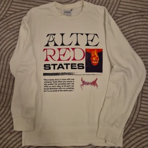 Vit sweatshirt med tryck från Elektra - Säljer en vit sweatshirt från Elektra med ett stort tryck på framsidan i svart och rött. Texten 'ALTE RED STATES' och en bild ger tröjan en unik look. Perfekt för dig som vill ha något annorlunda i garderoben.