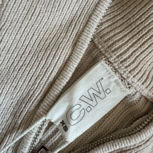 Beige zip tröja med dragkedja från Carin wester - Säljer en stilren beige ribbad tröja från C.W. med dragkedja vid halsen. Tröjan har långa ärmar och en hög krage men är lite croppad i modellen. Passar bra till både jeans och kjol. 🧥✨använd men i fint skick!