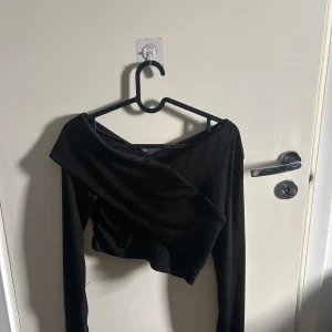 Svart offshoulder topp från Cider - Snygg svart offshoulder topp från Cider i glittrigt material. Toppen har en croppad passform och långa ärmar, perfekt för en kväll ute. Den unika designen ger en trendig look.