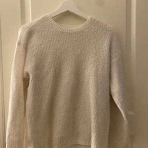Vit stickad tröja från 157 - Säljer en mysig vit stickad tröja från 157. Tröjan har en rund halsringning och långa ärmar, perfekt för kyligare dagar. Den är enkel och stilren, vilket gör den lätt att matcha med olika outfits. Perfekt för både vardag och avslappnade tillfällen. Jag skulle säga att den är rätt så stor i storleken.