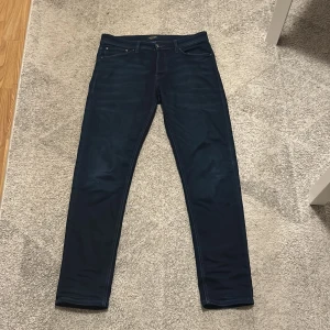 Mörkblå Jack & Jones jeans - Snygga mörkblå jeans från Jack & Jones med en klassisk design. De har en normal passform och är perfekta för en stilren look. Jeansen har fem fickor och stängs med knappar.