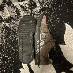 Premiata skor nyskick!! - Snygga bruna sneakers i mocka med ett unikt mönster på sidan. Skorna har snörning och en svart sula som ger en cool kontrast. Perfekta för en avslappnad stil. Dem är storlek 40 me passar till och med 42