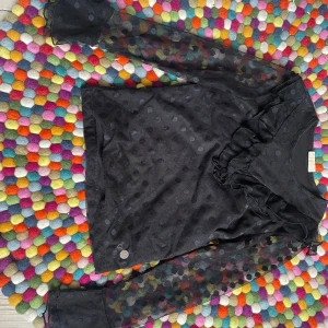 Svart prickig blus från Ü - Säljer en elegant svart blus från Ü med prickigt mönster. Blusen har långa, transparenta ärmar och volangdetaljer vid halsen. Perfekt för att ge en stilfull touch till din outfit 💕