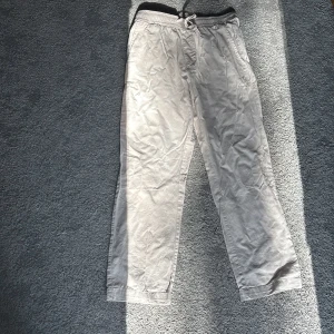 Beige linnebyxor med snörning - Säljer ett par bekväma beige linnebyxor med elastisk midja och snörning. Perfekta för en avslappnad dag hemma eller en snabb tur till affären. Byxorna har en lös passform och är gjorda i ett mjukt material.
