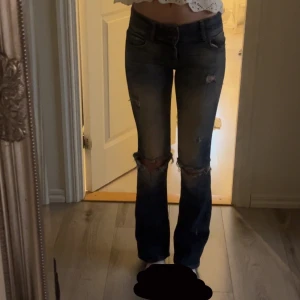 Blå bootcut jeans - Snygga blå bootcut jeans med slitna detaljer. De har en låg midja och en klassisk femficksdesign. Köpta i Lobdon för ca 400-500kr, jag har gjort egna hål i men dock nästan oanvända. Sitter jättebra på mig som har storlek xs-s/waist 23-24! 💕