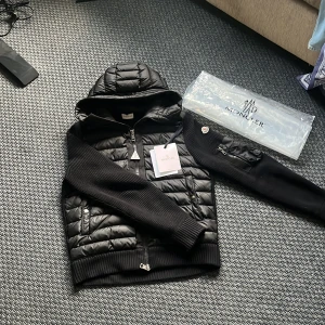 Svart jacka från Moncler - Säljer en snygg svart jacka från Moncler med quiltad design och huva. Jackan har långa ärmar och dragkedja framtill. Perfekt för kyligare dagar.