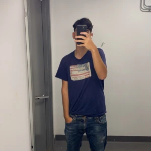 Ralph lauren Mörkblå t-shirt med tryck - Säljer en mörkblå t-shirt med ett tryck av en amerikansk flagga på bröstet. T-shirten har en avslappnad passform och är perfekt för en casual look. Passar bra till jeans eller shorts.