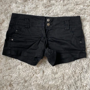 Svarta shorts med knappar - Snygga svarta shorts med två knappar framtill och fickor både fram och bak. De är låga i midjan. Säljer då de tyvärr inte kommer till användning längre. Jag tror de är strl 36 men lappen har tynat bort lite så det är svårt att se. Skriv till mig för fler bilder!💕