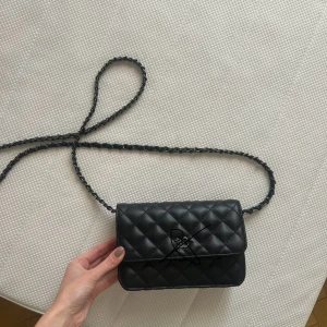 Svart quiltad axelväska - Snygg svart quiltad axelväska med en elegant kedjerem. Perfekt för att ge din outfit en stilfull touch. Skriv för bilder utan ritat på.