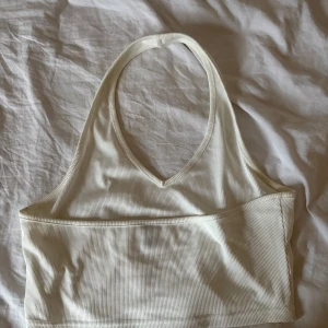 Vit ribbad linnetopp  - Säljer en stilren vit ribbad linnetopp från Shein. Toppen har en halterneck-design och är perfekt för varma dagar. Den är ärmlös och har en bekväm passform. Perfekt för att matcha med jeans eller kjol.