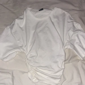 Vit t-shirt från Gina Tricot - Säljer en stilren vit t-shirt från Gina Tricot i storlek XXS. T-shirten har en unik rynkad detalj på sidan som ger en snygg twist. Perfekt för en casual look eller att styla upp med accessoarer. 🖤