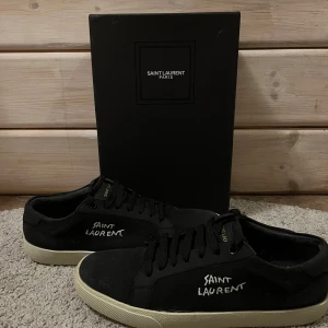 Svarta sneakers från Saint Laurent - Snygga svarta sneakers från Saint Laurent med vit logga på sidan. Skorna har en klassisk design med snörning och en vit sula. Perfekta för en stilren look.
