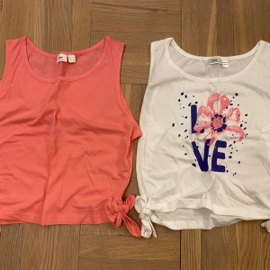 Två ärmlösa linnetoppar med knyt. Nyskick! Stl. Xs - Nyskick! Aldrig använda, men tyvärr ingen lapp kvar. Säljer två ärmlösa linnetoppar. Den ena är vit med ett färgglatt tryck av en blomma och texten 'LOVE', medan den andra är i en härlig korallfärg. Båda topparna har knytning i sidorna för en extra detalj. 