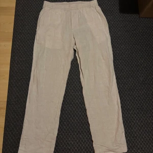 Beige linnebyxor från H&M - Säljer ett par bekväma beige linnebyxor med elastisk midja. Perfekta för en avslappnad stil och sköna att bära under varma dagar.