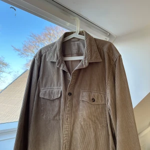 Beige overshirt från Marc O'Polo - Snygg beige overshirt från Marc O'Polo i manchester. Skjortan har långa ärmar och två bröstfickor med knappar.
