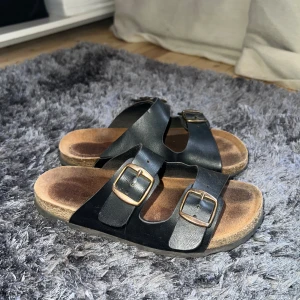 Svarta sandaler med spännen - Snygga svarta sandaler med dubbla justerbara spännen i metall. Perfekta för en avslappnad stil under varma dagar. Sandalerna har en bekväm fotbädd och en slitstark sula.