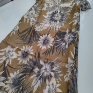 Blommig klänning från Prêt (Siden) - Säljer en elegant blommig klänning från Prêt i 100% silke. Klänningen har korta ärmar och ett vackert blommönster i beige och grå toner. Perfekt för en stilfull look.