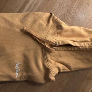 ” Orange” hoodie från New Black - Säljer en snygg gul/orange  hoodie från New Black med broderad logga på bröstet. Den har en klassisk design med dragsko i huvan och ribbade muddar vid ärmslut och nederkant. Perfekt för en avslappnad stil! Frakt betalas av köpare 