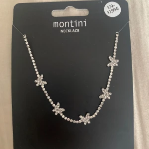 Silverfärgat halsband med stjärnor från Montini - Elegant silverfärgat halsband från Montini dekorerat med glittrande fjärilar. Halsbandet har en justerbar kedja för perfekt passform aldrig andvänd.