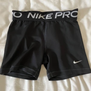 Svarta Nike pro Shorts  - Säljer ett par svarta Nike Pro träningsshorts med elastisk midja och vit logga. De har några tydligare defekter som att midjan rullats ner och stygnen gått upp där bak men säljes pga för liten storlek🥰