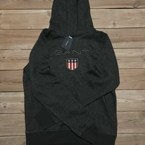 Mörkgrå hoodie från GANT - Säljer en snygg mörkgrå hoodie från GANT.                Storlek 176, passar xs kanske S. Aldrig använd, Lappen Kvar.                                                       Nypris 799kr