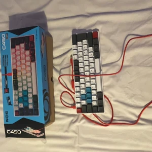Flerfärgat mekaniskt tangentbord C450 helt nytt  - Säljer ett mekaniskt tangentbord från NOS, modell C450. Tangentbordet har en färgglad design med vita, svarta, röda och blå tangenter. Det ansluts via en röd USB-kabel. Perfekt för gaming eller kontorsarbete!