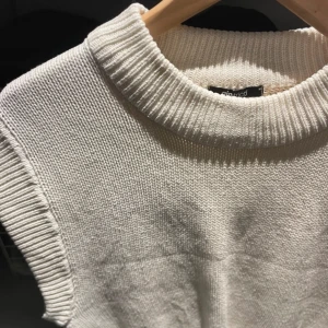 Vit stickad ärmlös topp - Säljer en stilren vit stickad topp med ribbad krage och nederkant. Köpt på vinted men har tyvärr aldrig använts. Kan användas som väst över annan tröja eler bara som den är 