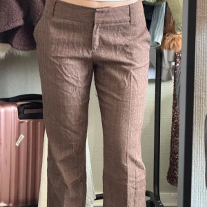 Bruna kostymbyxor - Snygga bruna kostymbyxor med en klassisk passform. Byxorna har en rak stil och är perfekta för en stilren look. De har en diskret dragkedja och knappar framtill. Lite skrynkliga pga legat i garderoben men fixas lätt med en liten steam!