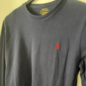 Mörkblå långärmad tröja från Ralph Lauren - Säljer en stilren mörkblå långärmad tröja från Ralph Lauren med det klassiska röda broderade logotypen på bröstet. Perfekt för en avslappnad och snygg look. Tröjan har en rund halsringning och är gjord i mjukt bomullsmaterial. Nypris: 999kr
