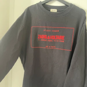 Svart tröja från Zadig & Voltaire - Säljer en svart tröja från Zadig & Voltaire med röd text och detaljer på framsidan. Tröjan har en rund halsringning och långa ärmar. Perfekt för en stilren och avslappnad look. Nypris: 4599kr. 