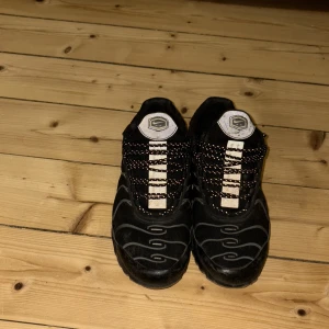 Nike Air Max Plus TN svarta sneakers - Säljer ett par svarta Nike Air Max Plus TN sneakers med vita och grå detaljer samt reflekterande partier. Skorna har snörning och en tydlig TN-logga bak. Perfekta för dig som gillar streetwear och sportig stil.priset är ej hugget i sten