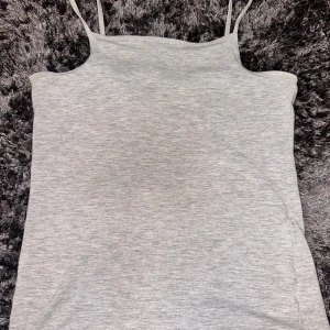 Ljusgrått linne med smala axelband - Säljer ett ljusgrått linne med smala axelband. Toppen är enkel och stilren, perfekt att matcha med olika outfits. Mjukt material och figurnära passform. Använd ett fåtal gånger.