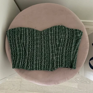 Grön tubtopp med vita prickar - Säljer en grön tubtopp med vita prickar och vertikala sömmar. Toppen är axelbandslös och har en snygg, figurnära passform. Perfekt att styla till både jeans och kjol för en trendig look.