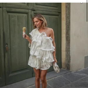 Lojsan Wallin x NA-KD miniklänning med spets och volanger - Superfin vit kortklänning i spets med stora volangdetaljer och oneshoulder-design. Klänningen har en luftig passform och är perfekt för sommarens alla tillfällen. Snygg och unik look som verkligen sticker ut! Säljer pga för stor, provad 2 gången prislapp och original förpackning kvar