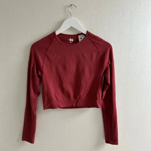 Röd croppad träningströja - Säljer en röd croppad långärmad träningstopp. Tröjan är i ett stretchigt syntetmaterial och har en tight passform. Den har diskreta ribbade detaljer på ärmarna. Helt ny med prislapp kvar💕💕