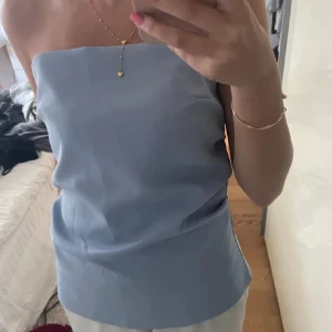 Ljusblå tubtopp - Säljer en stilren ljusblå tubtopp. Toppen är axelbandslös och har en enkel, rak design som passar perfekt till sommaren. 
