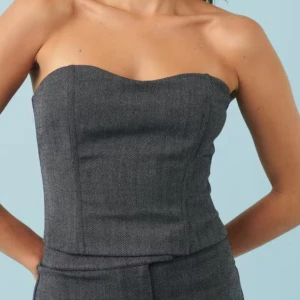 Mörkgrå tubtopp i kostymtyg - Säljer en stilren mörkgrå tubtopp i kostymtyg med smockad rygg för extra komfort. Toppen har en figurnära passform och en lätt hjärtformad urringning framtill. Perfekt att matcha med kostymbyxor eller kjol.