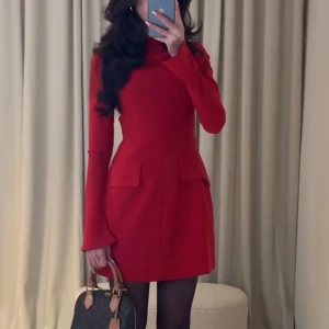 Röd långärmad kortklänning - Säljer en stilren röd klänning med lång ärm och figurnära passform. Klänningen har hög hals och två dekorativa fickor framtill. 